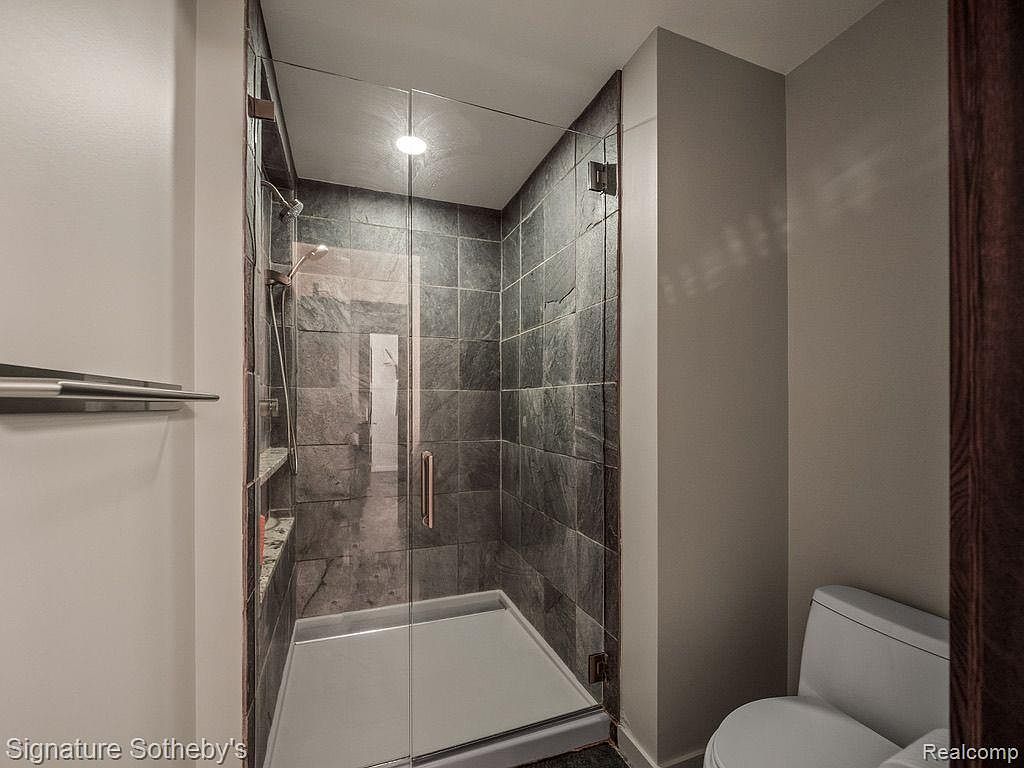 This is a bathroom featuring a glass-enclosed shower with dark gray tile and a light gray shower base. The walls outside the shower are painted a neutral gray, and a toilet is visible in the corner. The overall impression is modern and clean.