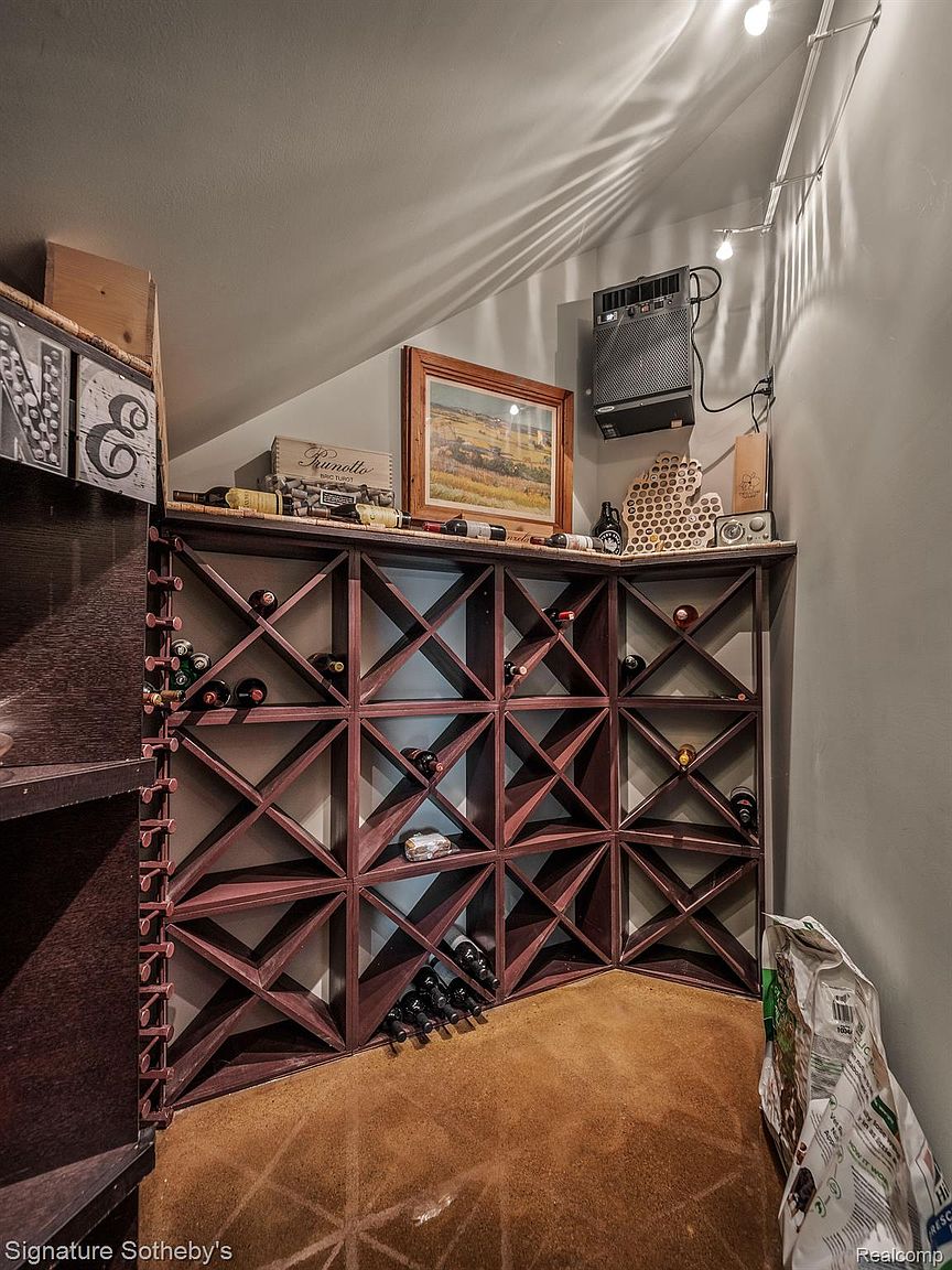 This image showcases a cozy wine cellar featuring a custom-built wooden wine rack filled with various bottles. The room has a warm, inviting ambiance with a carpeted floor and a collection of decorative items displayed on top of the rack. The space is well-organized and designed for wine storage and display.