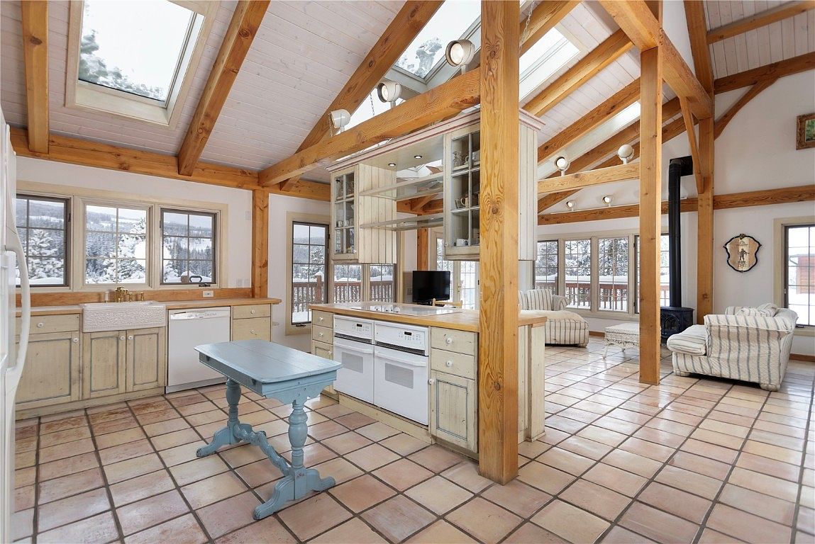 This interior shot showcases a spacious kitchen with a rustic-chic design. Exposed wooden beams support the high ceiling, complemented by light-colored cabinetry and a central island. The kitchen features modern appliances and a tiled floor, creating a warm and inviting atmosphere.