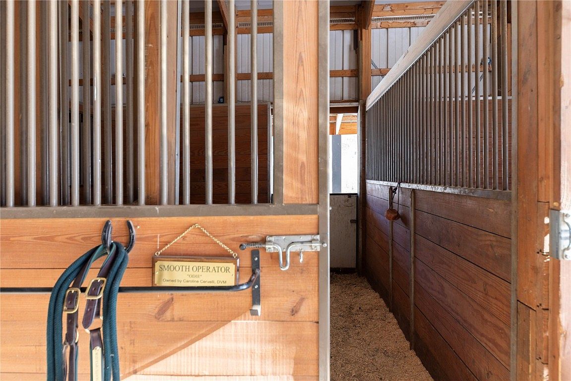 This image showcases the interior of a horse stall, featuring wooden walls and metal bars. A sign reading "SMOOTH OPERATOR" is mounted on the wall, along with horse tack. The stall appears clean and well-maintained, suggesting a comfortable and functional space for horses.
