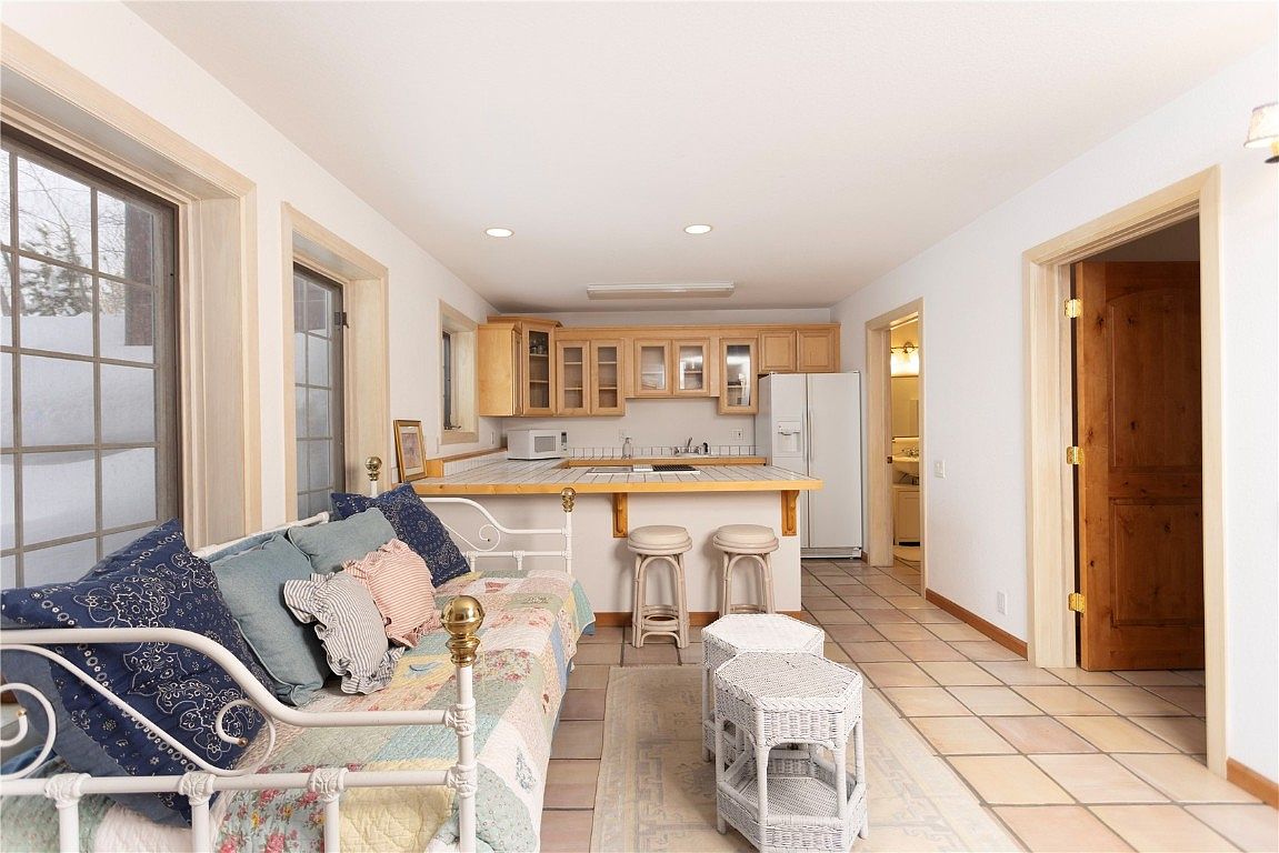 This interior shot showcases a cozy kitchen and living area. The kitchen features light wood cabinetry, a tiled countertop with bar seating, and white appliances. Adjacent to the kitchen is a living space with a daybed adorned with colorful pillows and a quilt, creating a warm and inviting atmosphere.