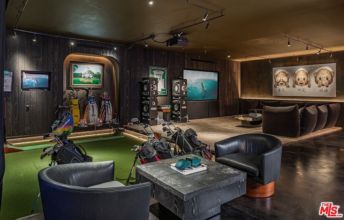 This sophisticated basement entertainment space features a dedicated indoor golf simulator area complete with putting green and multiple golf bags. The room is designed with a moody, masculine aesthetic, featuring dark wood-paneled walls, plush leather seating, and a large sectional sofa facing a projection screen. The cinematic perspective captures the seamless blend of a high-end lounge and a private sports training facility.