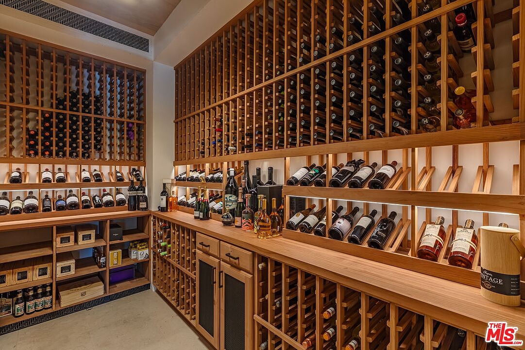 This sophisticated custom wine cellar features extensive floor-to-ceiling wooden racking systems designed to showcase a large collection of bottles. The space includes both horizontal display shelves and traditional angled racks, illuminated by integrated LED lighting that highlights the labels. The warm wood tones and organized layout create an inviting, high-end atmosphere perfect for wine enthusiasts.
