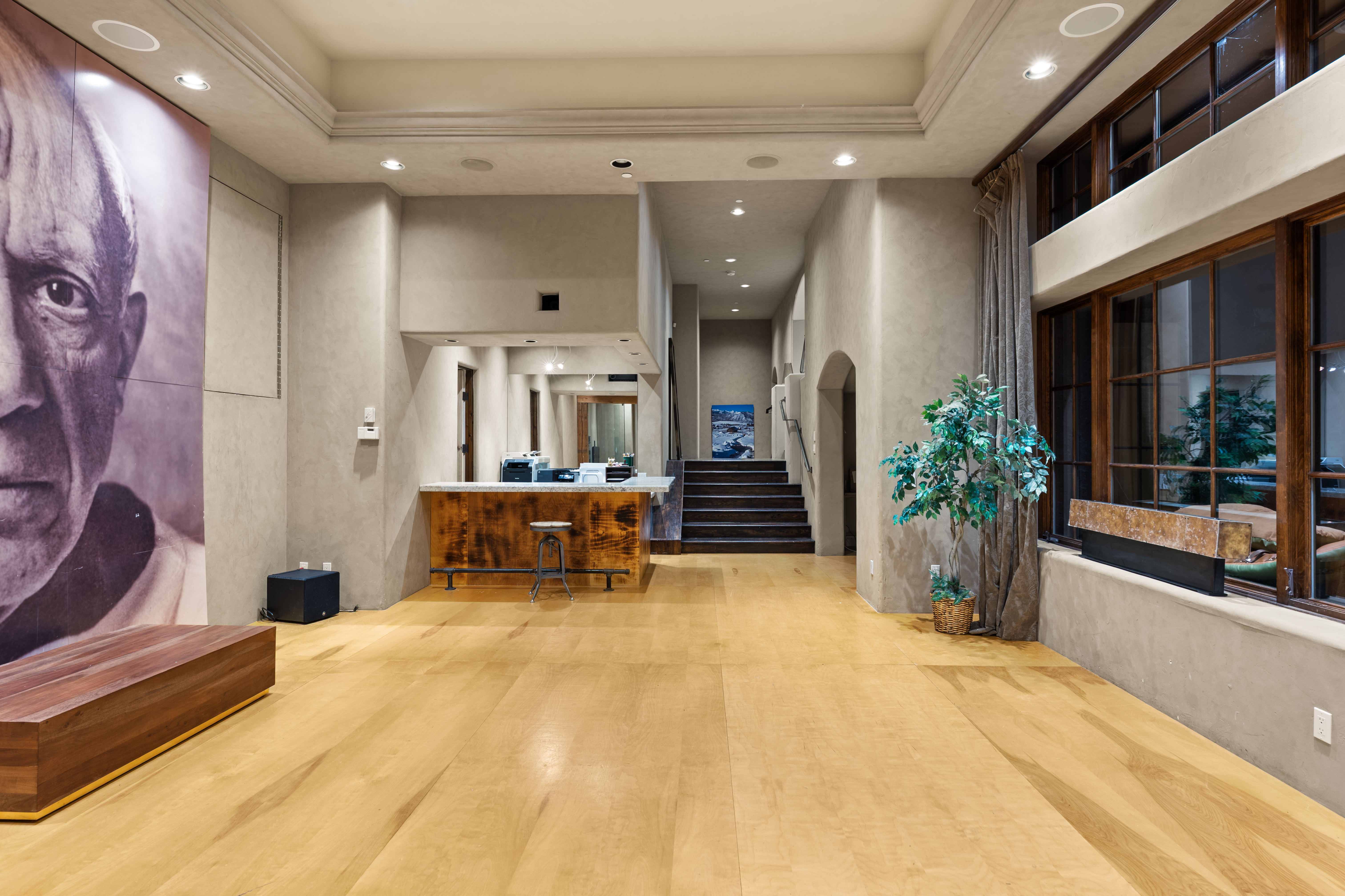This interior shot showcases a spacious hallway with light wood flooring and textured walls. A large portrait dominates one side, while a reception desk and staircase lead to other areas. The space is well-lit with recessed lighting, creating a welcoming and sophisticated atmosphere.