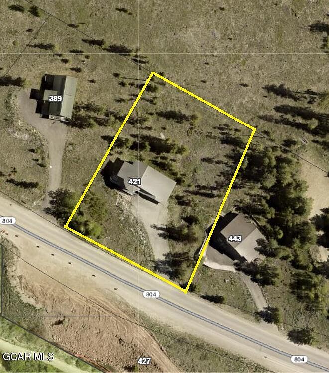 This aerial view showcases a property with multiple buildings, including structures labeled 389, 421, and 443. The property is bordered by a road marked as 804 and is surrounded by natural terrain with scattered trees and vegetation. A yellow outline defines the property boundaries, highlighting its size and location relative to the road and neighboring structures.