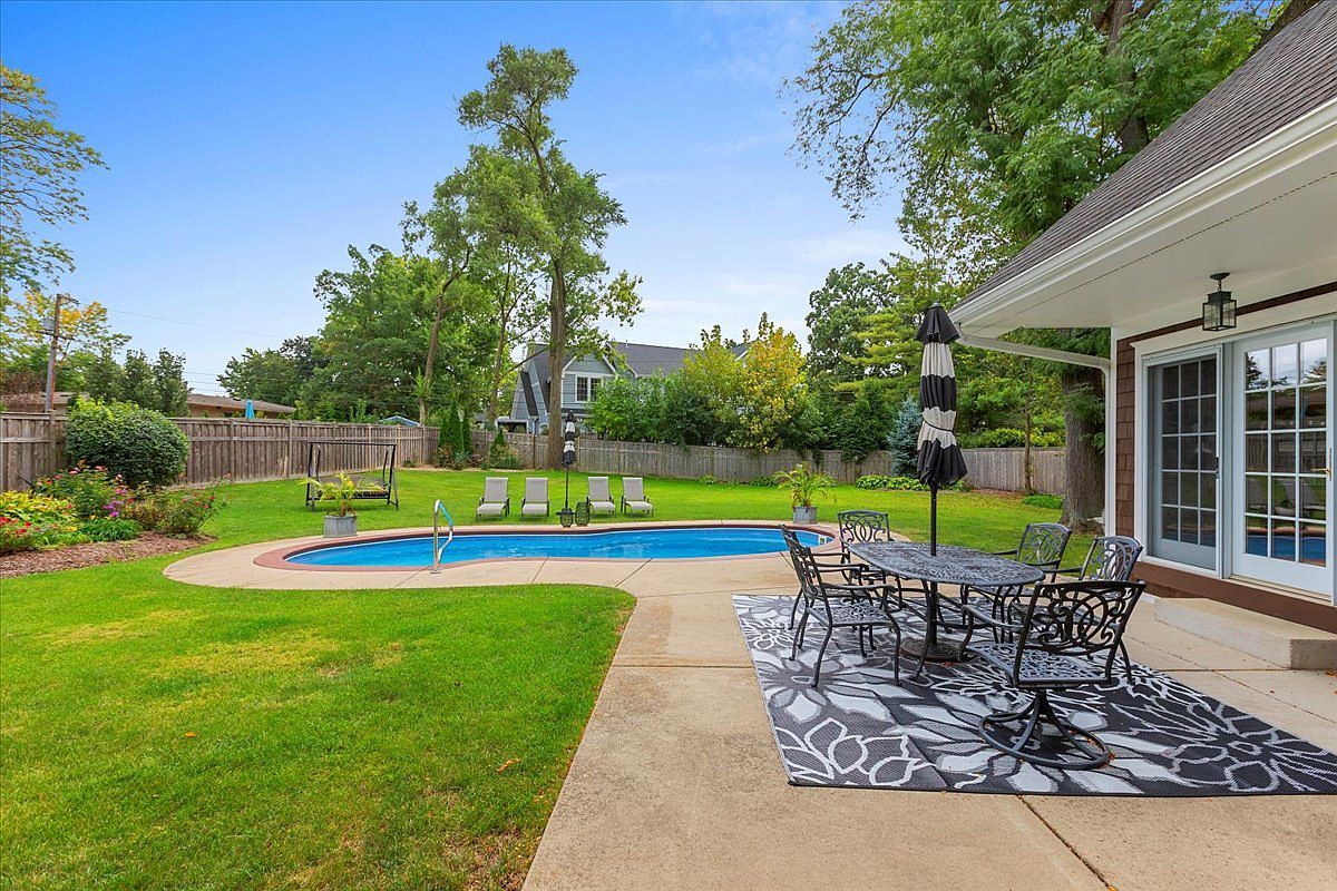 This image showcases a beautifully landscaped backyard featuring a private pool and patio area. The pool is surrounded by lush green grass and mature trees, creating a serene and inviting atmosphere. A patio set with an umbrella offers a comfortable space for outdoor dining and relaxation, enhancing the property's appeal for entertainment and leisure.