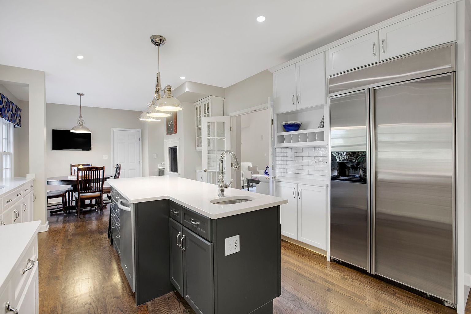 This is a well-lit kitchen featuring a dark gray kitchen island with a white countertop and a stainless steel sink. The kitchen also includes white cabinetry, stainless steel appliances, and hardwood floors. The perspective is from a medium distance, showcasing the island and surrounding kitchen elements.
