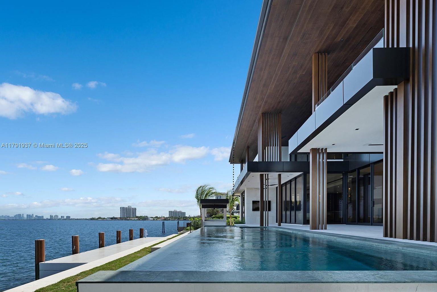This image showcases a luxurious modern home with a stunning infinity pool overlooking the water. The architectural design features clean lines, wood accents, and large glass windows, creating a seamless indoor-outdoor living experience. The pool's edge blends with the horizon, offering breathtaking views and enhancing the property's appeal.