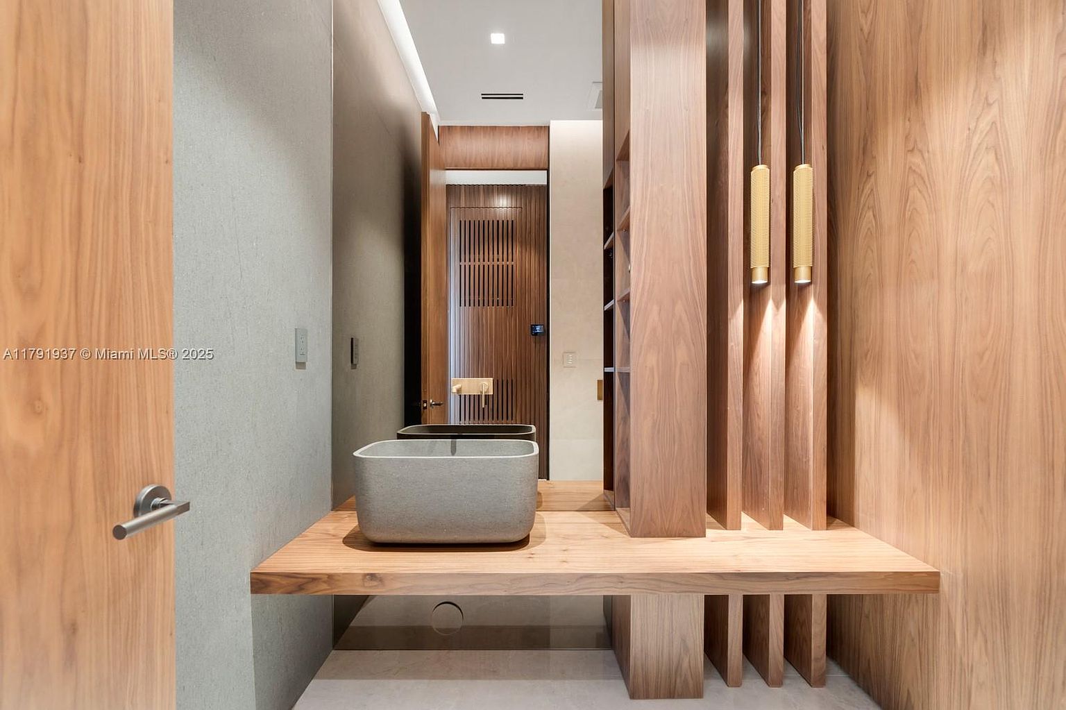 This is a modern bathroom featuring a floating vanity with a rectangular vessel sink. The vanity is made of wood and has a unique design with vertical supports. The walls are a combination of gray and wood paneling, and there are two pendant lights hanging from the ceiling. The overall style is minimalist and contemporary.