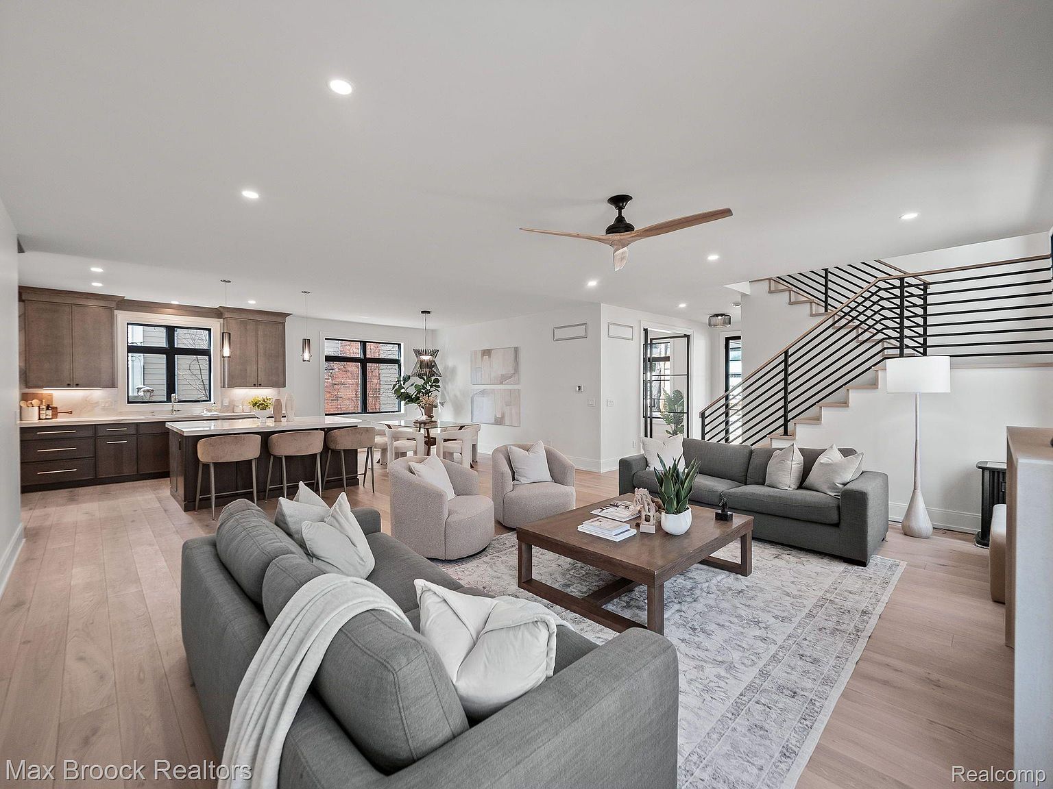 This is an interior shot of a modern living room that seamlessly blends into the kitchen and dining area. The living room features two gray sofas, a wooden coffee table, and a light-colored area rug. The open floor plan allows for easy flow between the living, dining, and kitchen spaces, creating a welcoming and spacious atmosphere.