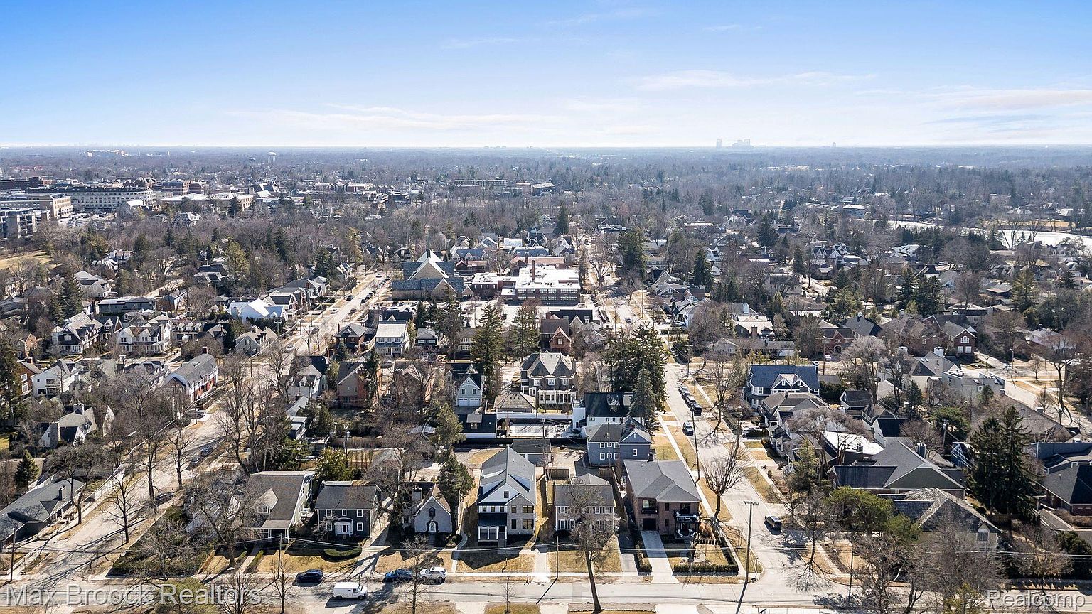 This aerial shot showcases a well-established residential neighborhood with a mix of architectural styles. The houses are neatly arranged along tree-lined streets, creating a picturesque and desirable community. The view extends to the horizon, revealing a sprawling cityscape in the distance.
