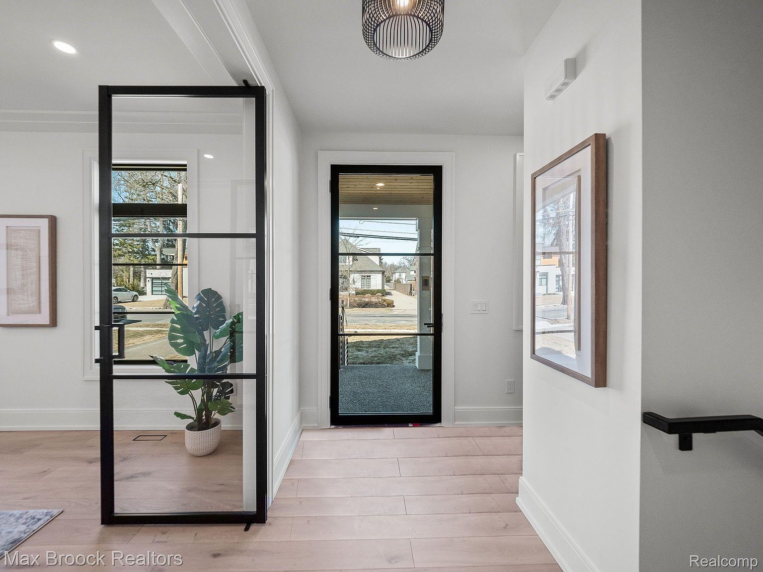 This interior shot showcases a bright and modern hallway with light wood flooring and white walls. A black-framed glass partition adds a contemporary architectural element, while a matching front door allows natural light to flood the space. The hallway leads to other rooms, creating a sense of flow and connectivity within the home.