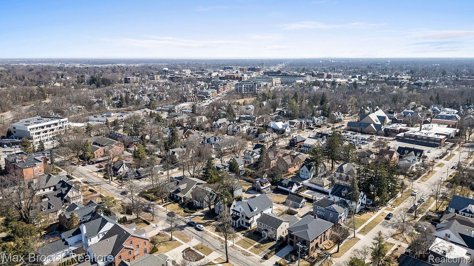 This aerial view showcases a charming residential neighborhood with a mix of architectural styles, mature trees, and well-maintained streets. The perspective provides a comprehensive overview of the area, highlighting the density of housing and the proximity to local amenities and green spaces. The clear blue sky enhances the overall appeal, suggesting a desirable and vibrant community.