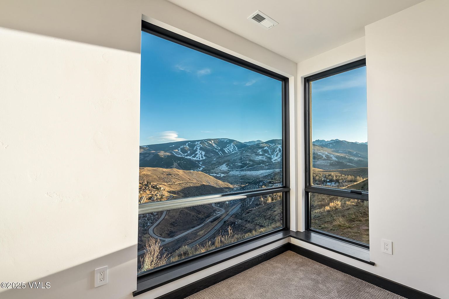 This interior shot showcases a bright room with large windows offering a stunning mountain view. The room features neutral-toned walls and carpet, creating a serene and inviting atmosphere. The black window frames provide a modern contrast, highlighting the scenic landscape and enhancing the room's appeal for potential buyers.