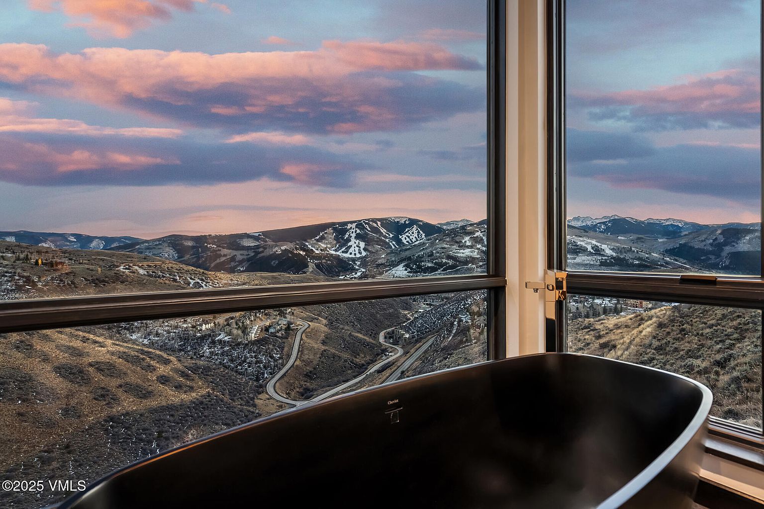 This image showcases a luxurious primary bathroom with a stunning view of snow-dusted mountains through large windows. A sleek, black freestanding bathtub is positioned to take full advantage of the scenery. The room exudes a sense of tranquility and high-end comfort, making it a desirable feature for potential buyers.