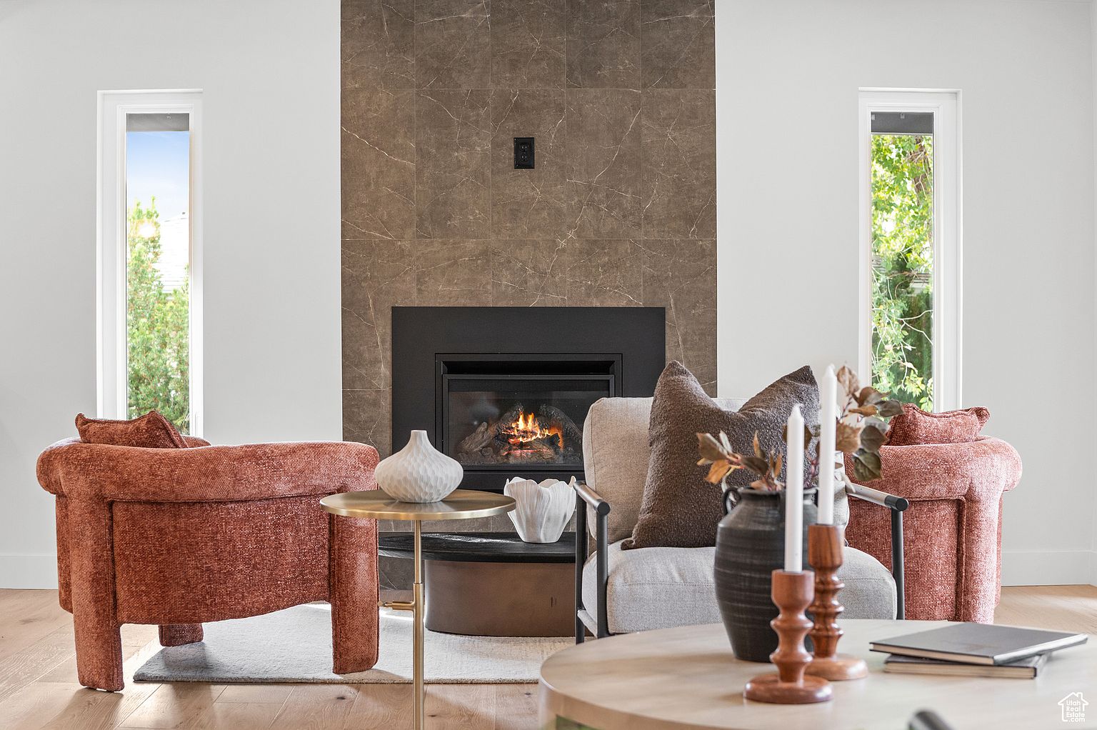 This interior shot showcases a stylish living room with a modern fireplace and two comfortable armchairs. The room is well-lit with natural light streaming through the windows, highlighting the neutral color palette and contemporary decor. A round coffee table and side table add functionality and visual interest to the space.