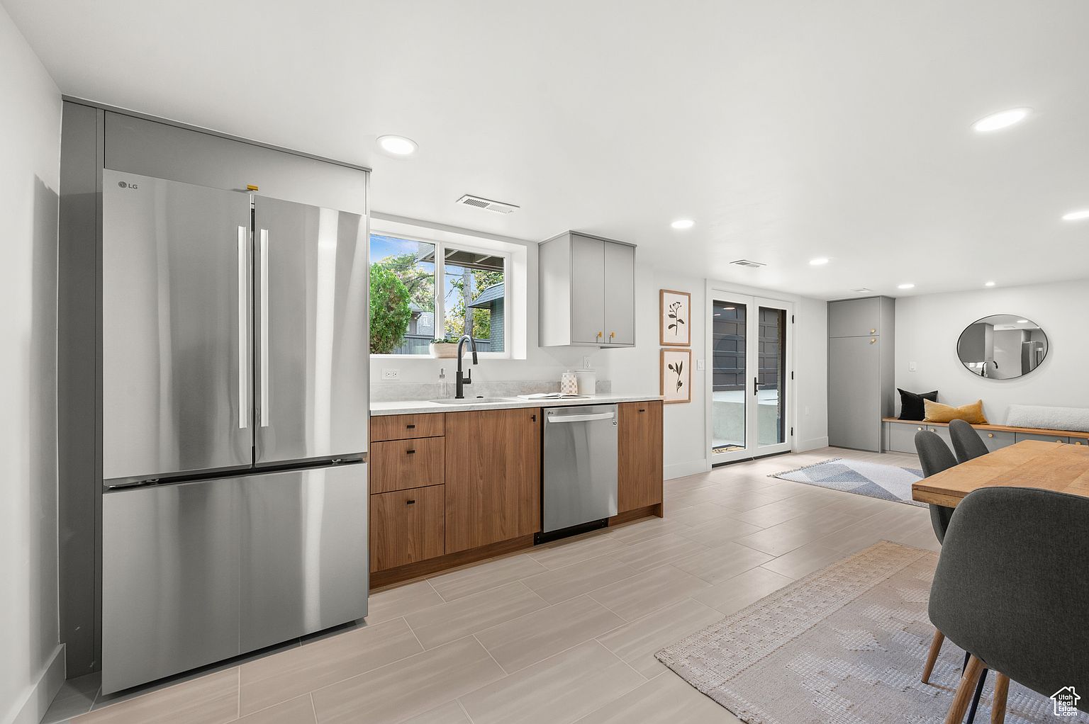 This is a well-lit, modern kitchen with a clean and spacious design. It features stainless steel appliances, including a large refrigerator and dishwasher, complemented by light gray upper cabinets and wood-toned lower cabinets. The kitchen seamlessly transitions into a dining area, creating an open and inviting space.