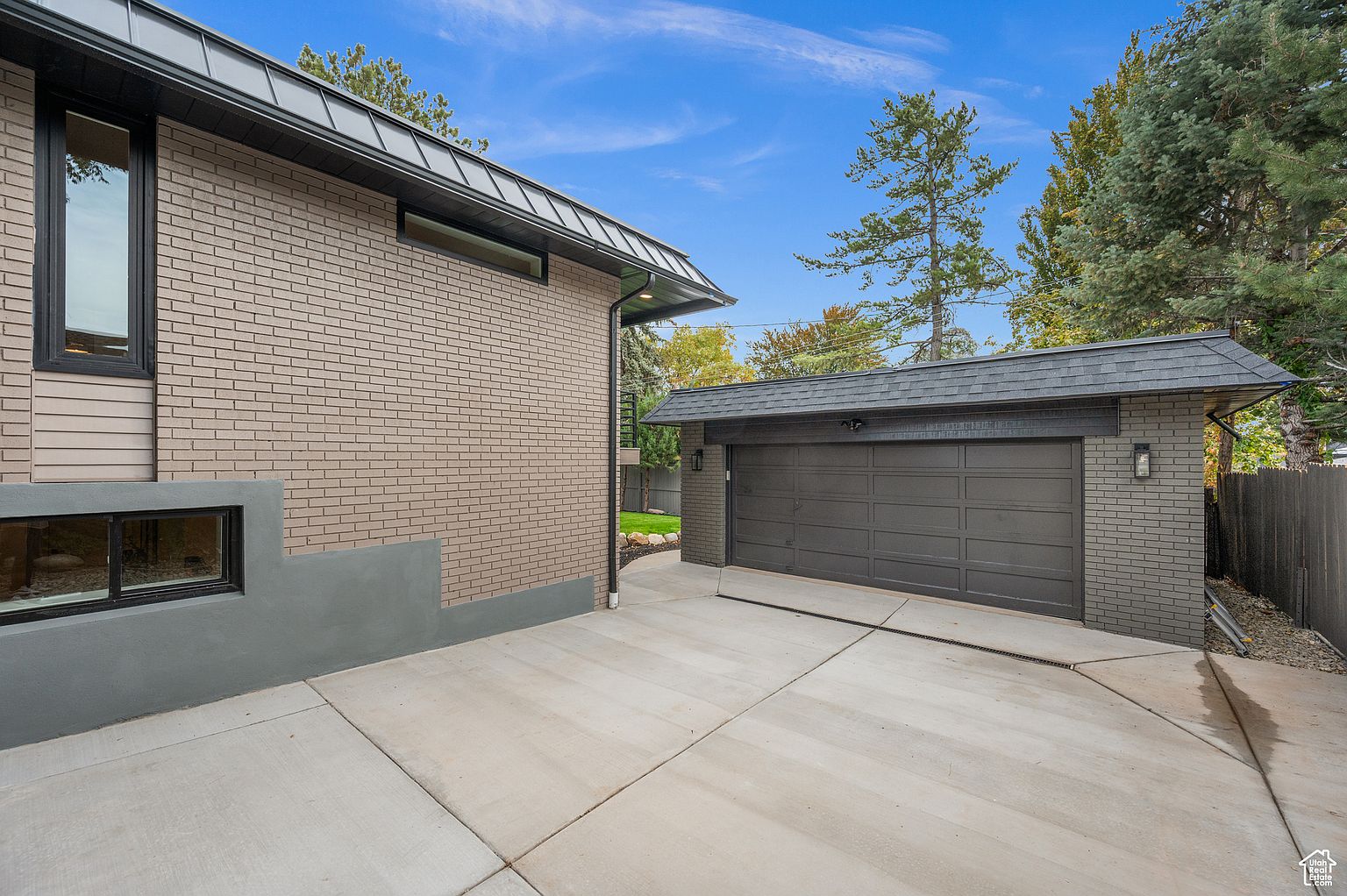 This image showcases the exterior of a modern home, focusing on the garage and driveway. The garage features a dark gray door and brick facade, complementing the main house's brickwork and dark trim. A spacious concrete driveway leads to the garage, offering ample parking space and enhancing the property's curb appeal.