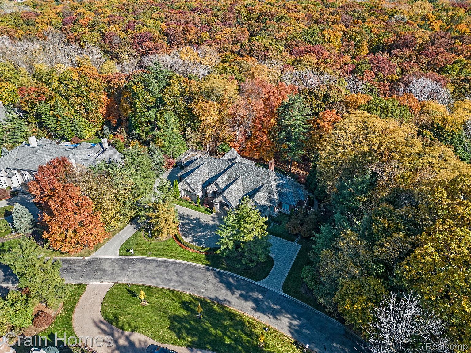 This aerial view showcases a luxurious home nestled amidst vibrant fall foliage. The property features a sprawling layout with a complex roofline, manicured lawns, and a circular driveway. The surrounding trees display a stunning array of autumn colors, creating a picturesque and private setting.