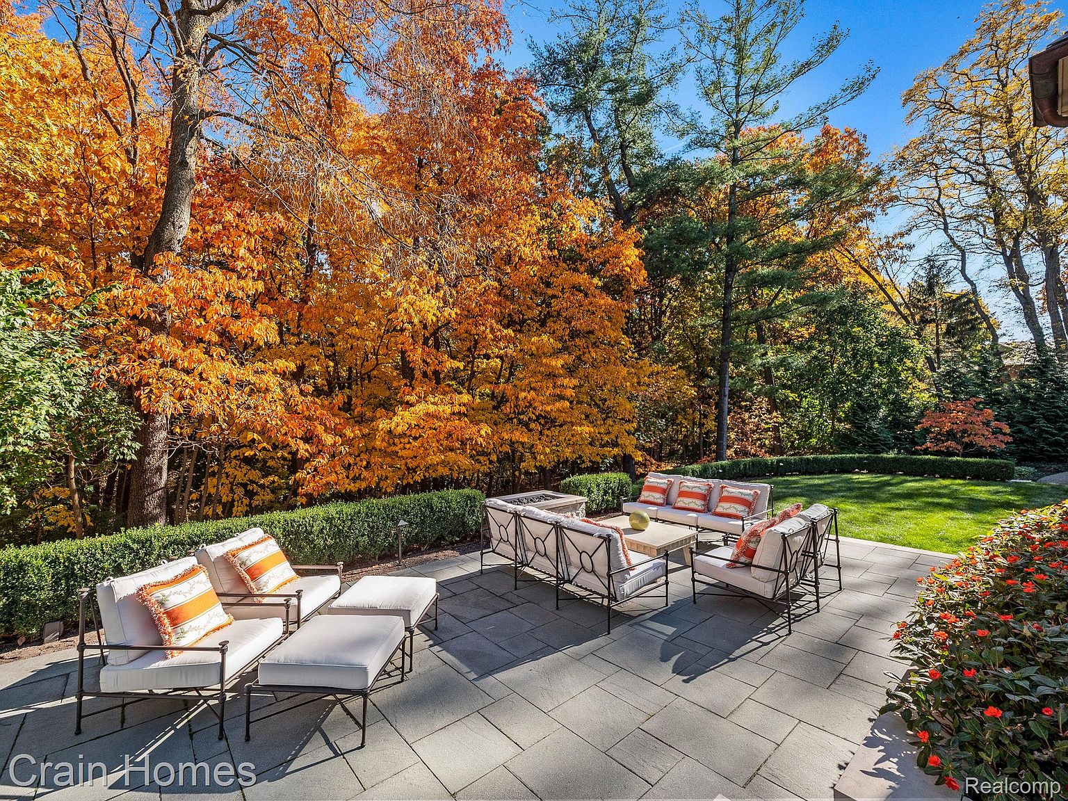 This image showcases a beautifully designed outdoor patio area, perfect for relaxation and entertaining. The patio features comfortable seating arrangements with stylish cushions and a central coffee table, all set on a paved stone surface. Lush greenery and vibrant autumn foliage create a serene and inviting atmosphere, enhancing the property's appeal.