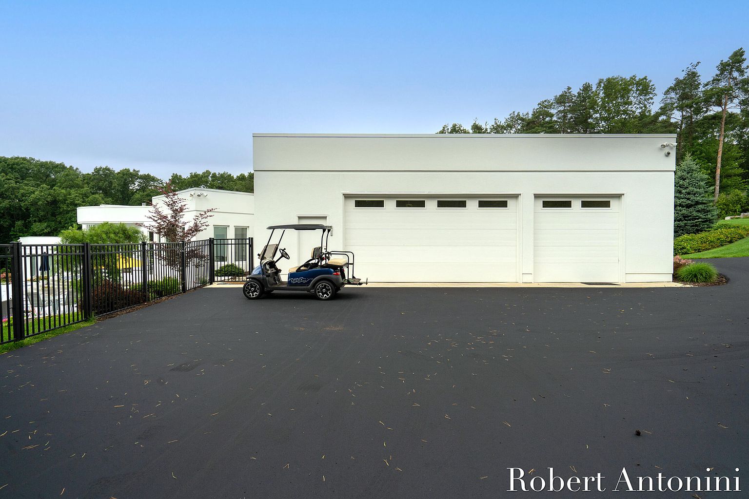 This image showcases a modern, two-car garage with a sleek, white exterior. The garage doors are paneled with horizontal windows near the top, adding a touch of contemporary design. A golf cart is parked nearby, and the driveway is paved with black asphalt, creating a clean and sophisticated look.