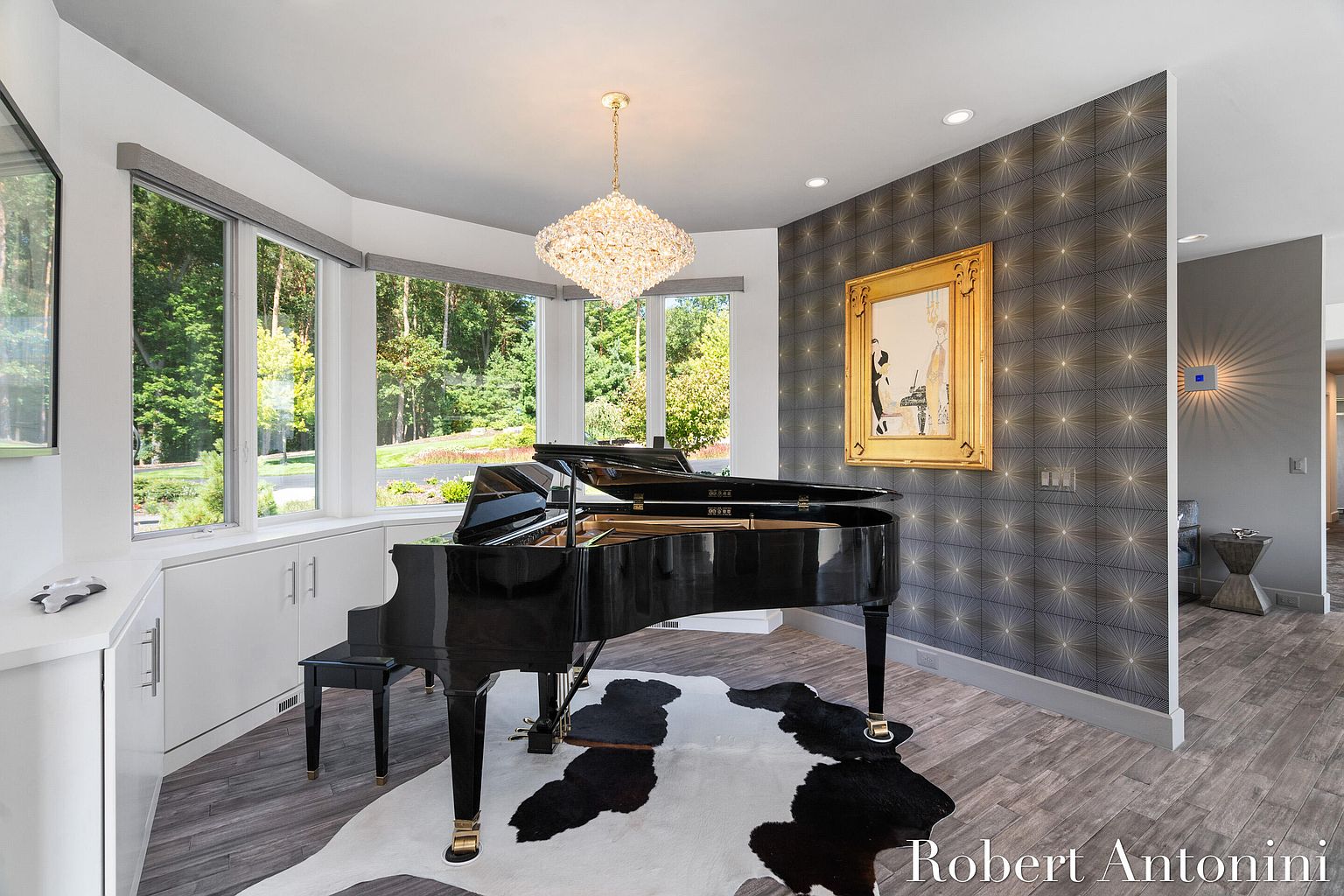 This elegant living room features a grand piano as its centerpiece, complemented by a striking black and white cowhide rug. A crystal chandelier adds a touch of luxury, while large windows offer views of the lush greenery outside. The room's design is a blend of classic and contemporary, creating a sophisticated and inviting atmosphere.