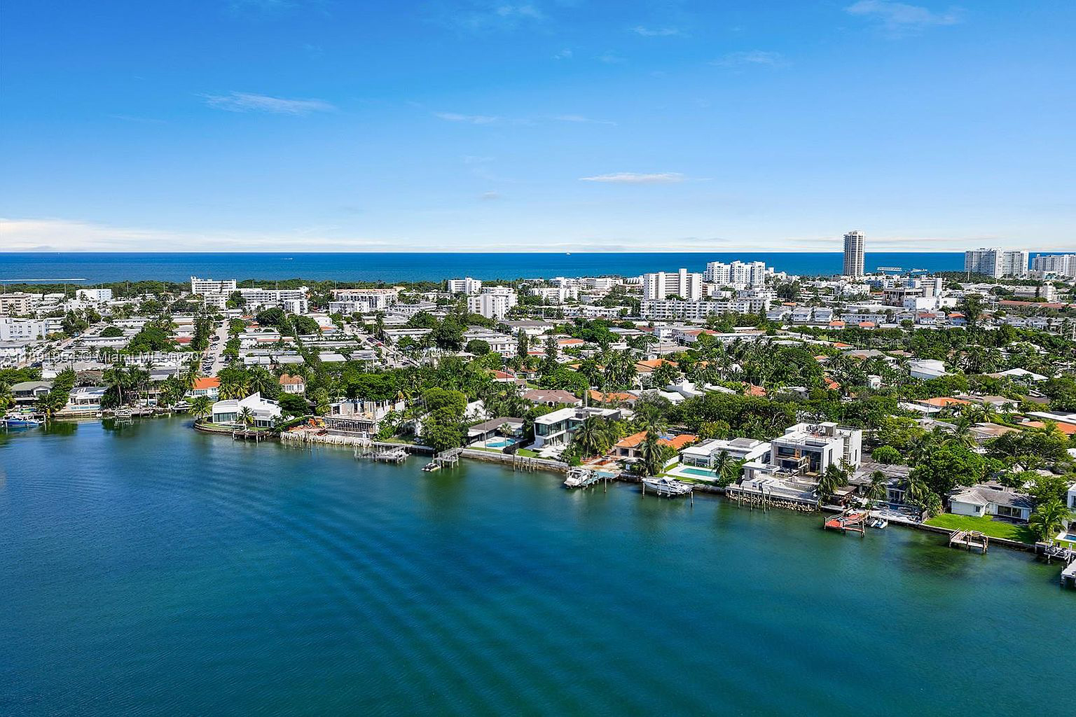 This aerial shot showcases an affluent waterfront property with luxurious homes lining the coastline. Lush landscaping, pools, and docks add to the appeal. The clear blue water and sky provide a stunning backdrop, emphasizing the desirable location of these residences.