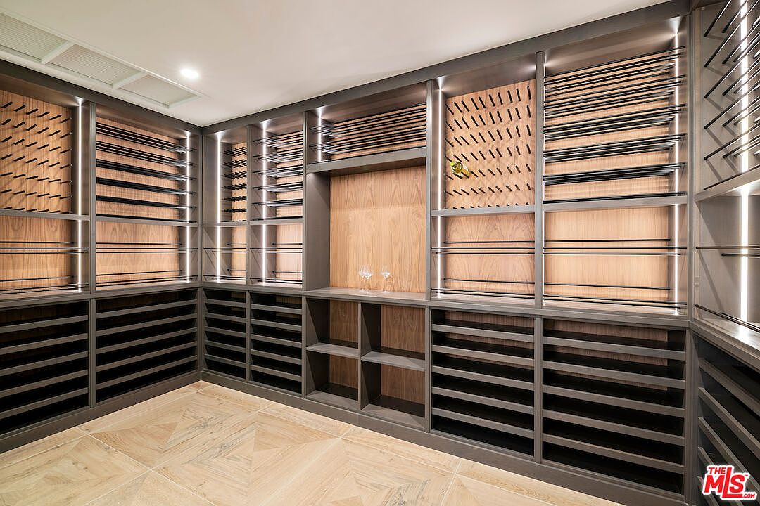 This sophisticated wine cellar features custom dark-toned cabinetry with integrated LED lighting that highlights the bottle storage racks. The room includes a central display area with a light wood back panel and a lower section with open shelving for additional storage. The space is finished with light-toned patterned wood flooring, creating a refined and organized atmosphere for wine collection.