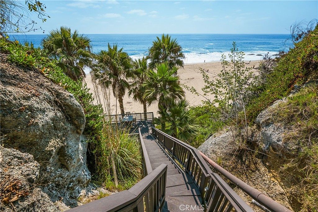 This image showcases a scenic outdoor area with a wooden staircase leading down towards a sandy beach and ocean. Lush greenery and palm trees surround the staircase, creating a tropical and inviting atmosphere. The view offers a direct access to the beach, enhancing the property's appeal for those seeking coastal living.