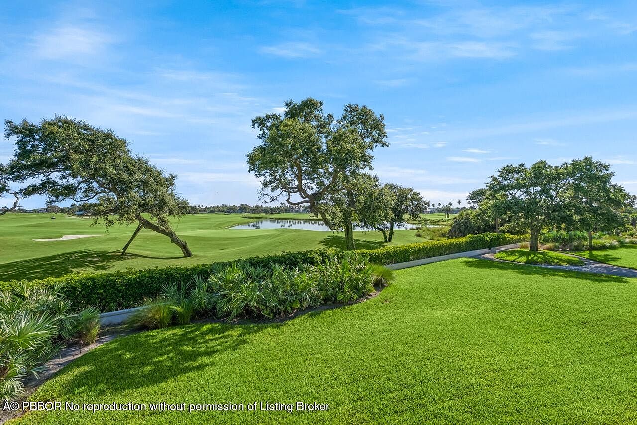 This image showcases a meticulously maintained yard or garden area, likely part of a larger estate or golf course community. Lush green grass, mature trees, and manicured hedges create a serene and inviting atmosphere. The view extends to a golf course with a water feature, suggesting a premium location and lifestyle.