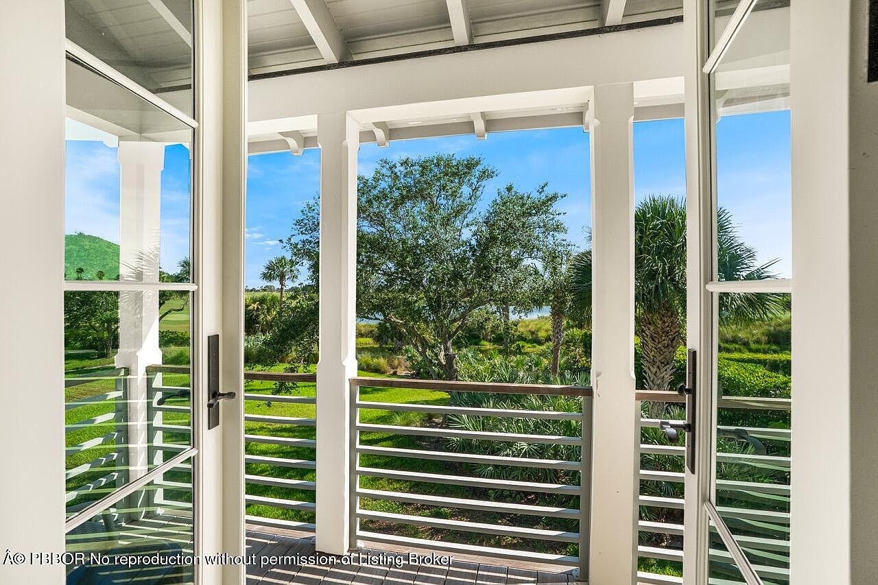This image showcases a charming patio or balcony with a view of a lush green landscape. The white railings and pillars create a clean and elegant aesthetic, framing the natural scenery beyond. The open doors invite a seamless transition between indoor and outdoor living, highlighting the property's appeal for relaxation and enjoying the surrounding environment.
