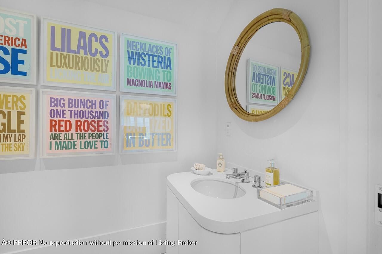This is a well-lit bathroom featuring a modern vanity with a curved design and an integrated sink. Above the vanity hangs a round mirror with a natural, possibly rattan, frame. The wall is adorned with a series of framed art prints, adding a touch of personality and color to the space.
