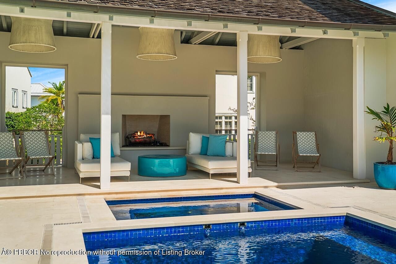 This image showcases a luxurious outdoor living space featuring a pool and a covered patio area. The patio includes comfortable seating around a fireplace, creating a cozy and inviting atmosphere. The pool's blue tiles contrast beautifully with the light-colored patio stones, enhancing the overall aesthetic appeal.