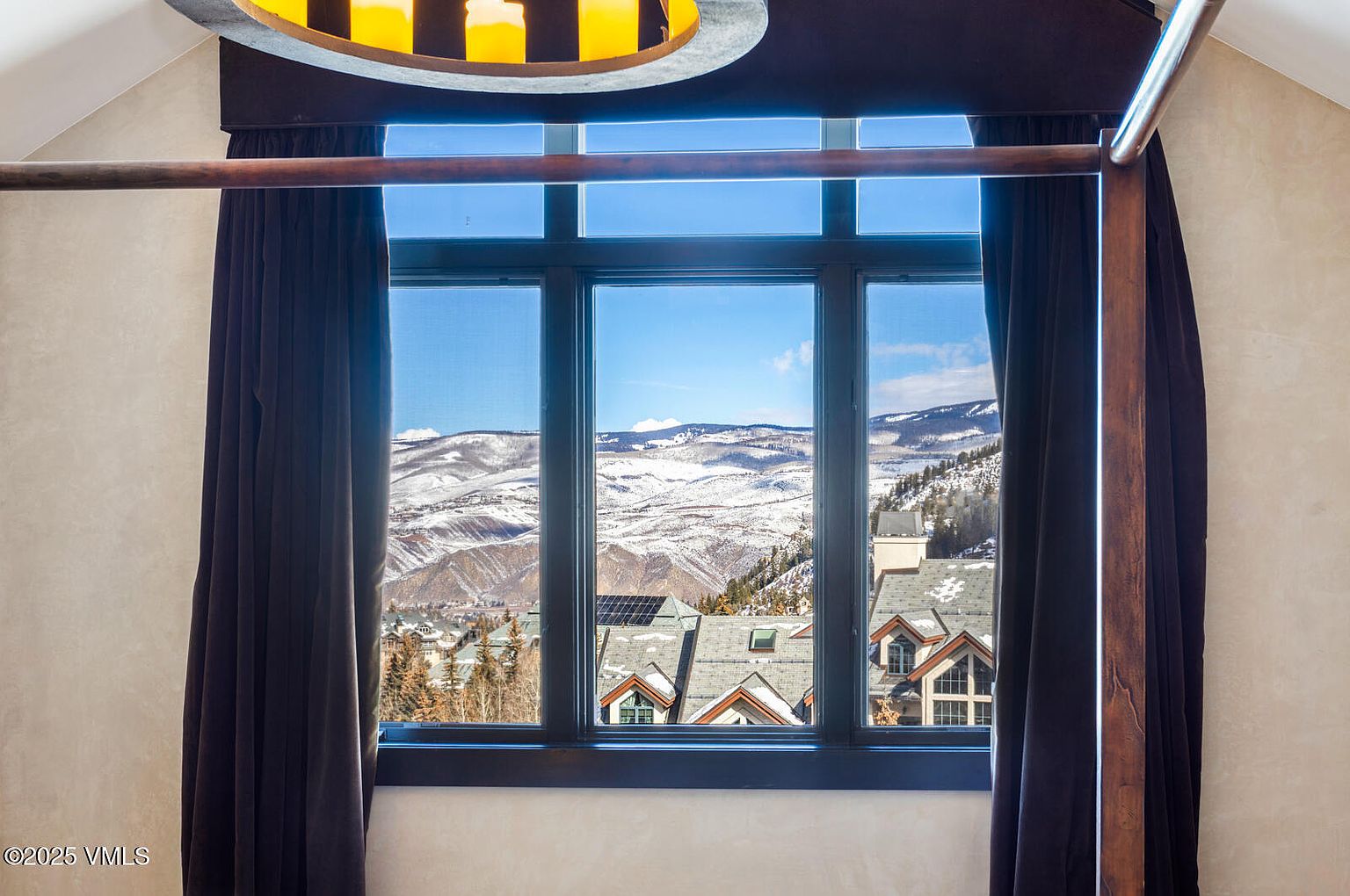 This image showcases a bedroom with a stunning view of snow-covered mountains through a large window. The room features dark curtains and a four-poster bed frame, adding a touch of elegance. The focus is on the scenic vista, emphasizing the property's desirable location and natural light.