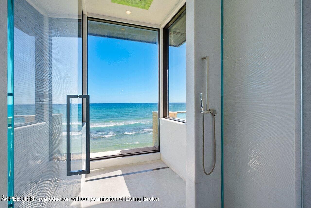This is a luxurious primary bathroom featuring a glass-enclosed shower with a stunning ocean view. The shower is equipped with modern fixtures, and the walls are adorned with textured white tiles. The open design and natural light create a spa-like atmosphere, perfect for relaxation.
