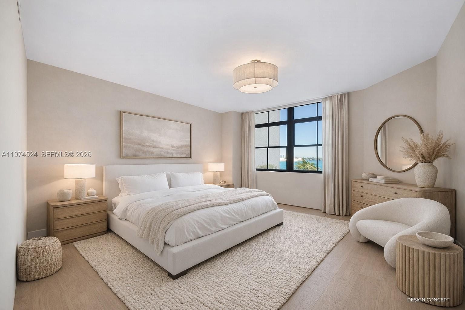 This serene primary bedroom features a neutral color palette with light wood flooring and a plush area rug. The room is anchored by a white upholstered bed flanked by matching light wood nightstands and table lamps, while a curved accent chair and a wooden dresser with a circular mirror complete the space. Large windows with floor-to-ceiling curtains provide natural light and a view of the outdoors, creating a calm and sophisticated atmosphere.