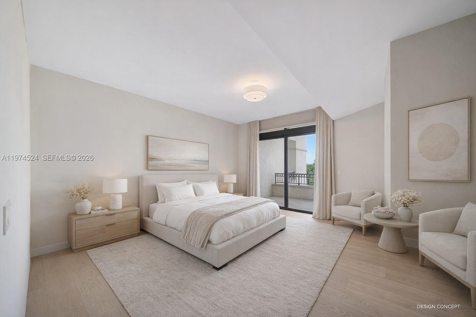 This serene primary bedroom features a neutral color palette, light wood flooring, and a large, plush bed centered against a wall adorned with abstract artwork. To the right, a cozy seating area with two armchairs and a small round table creates a relaxing nook, while large sliding glass doors provide access to a private balcony. The room is bathed in soft, natural light, creating an airy and sophisticated atmosphere.