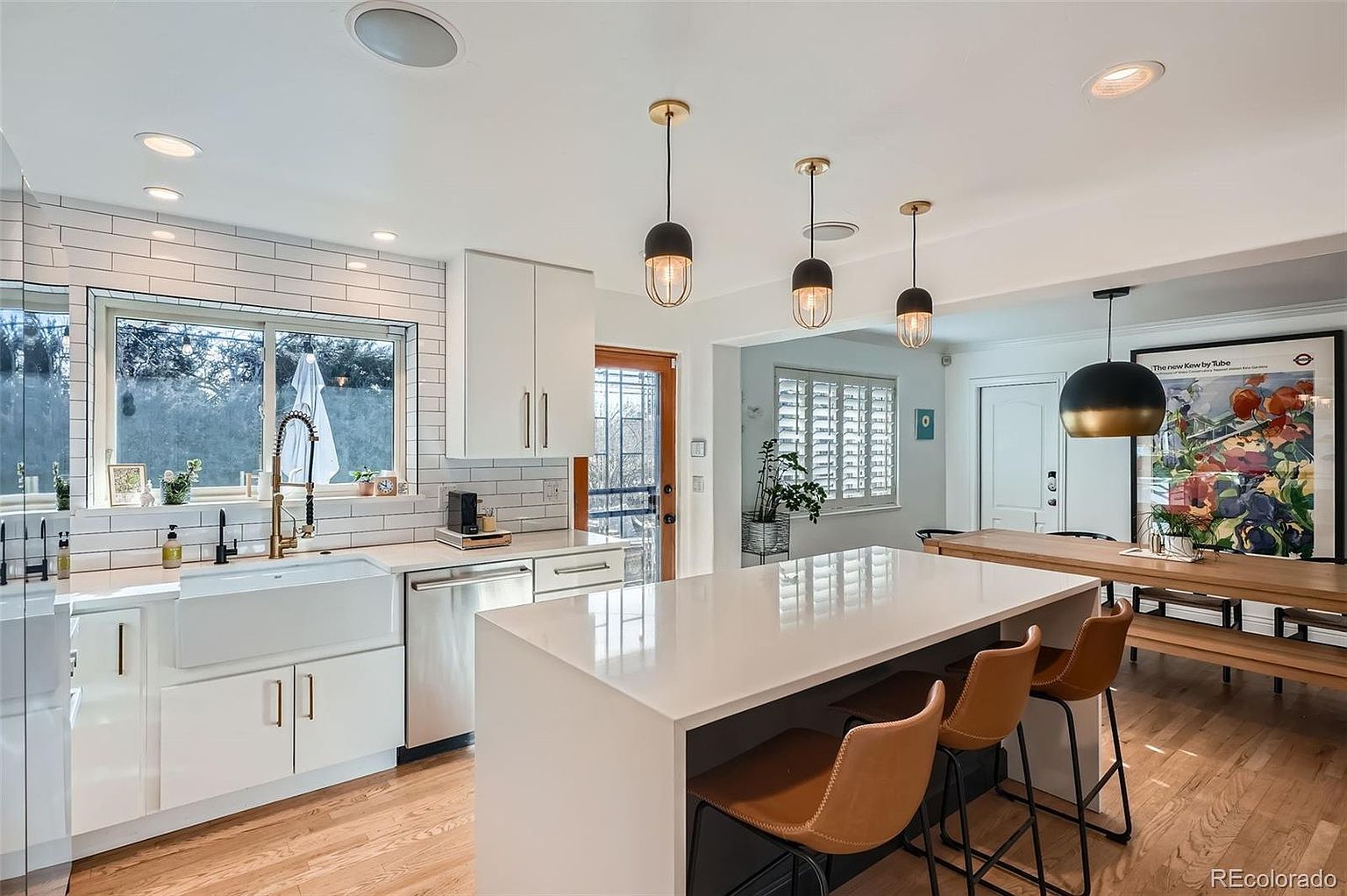 This is a bright and modern kitchen featuring white cabinetry, a farmhouse sink, and stainless steel appliances. A large island with seating provides ample counter space, and pendant lights add a touch of elegance. The hardwood floors and natural light create a warm and inviting atmosphere.