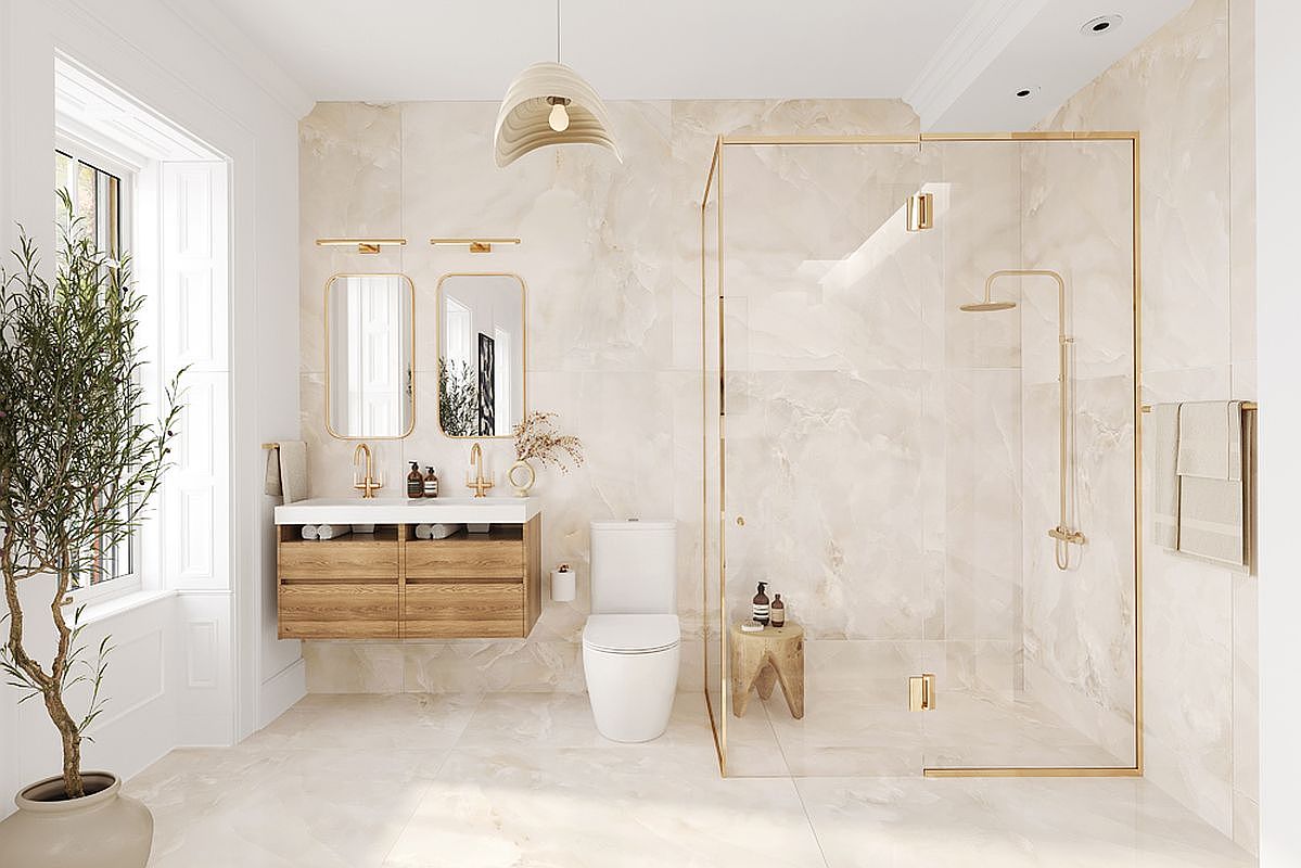 This is a luxurious primary bathroom featuring a double vanity with wooden cabinets, gold fixtures, and two rectangular mirrors. A glass-enclosed shower with gold trim and a rainfall showerhead adds to the spa-like atmosphere. The walls and floors are covered in light marble, creating a bright and elegant space.