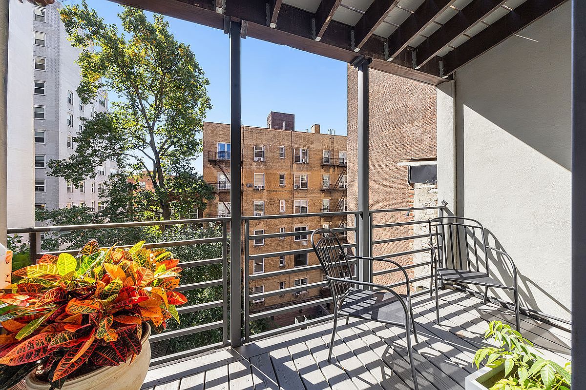 This image showcases a charming balcony with a view of neighboring buildings and lush greenery. The balcony features a wooden deck, metal railings, and comfortable seating, creating an inviting outdoor space. Potted plants add a touch of nature, enhancing the balcony's appeal and creating a relaxing atmosphere.