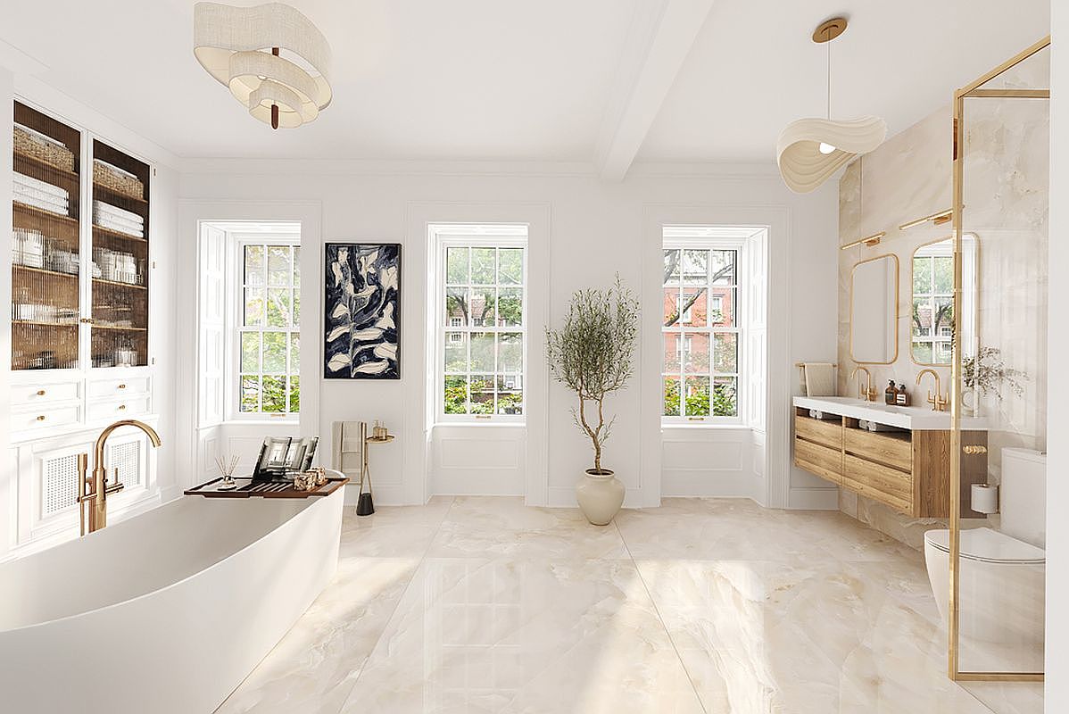 This is a luxurious primary bathroom featuring a freestanding bathtub with a gold faucet, a custom built-in cabinet with glass doors, and a floating vanity with double sinks. The room is illuminated by modern pendant lighting and natural light from three large windows. The flooring is a polished marble, creating a bright and elegant space.