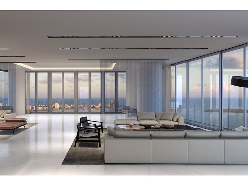 This is a spacious and luxurious living room with floor-to-ceiling windows offering panoramic ocean and city views. The room features modern furniture, including a large sectional sofa, armchairs, and a sleek coffee table. The open floor plan and minimalist design create a sophisticated and airy atmosphere, perfect for upscale living.