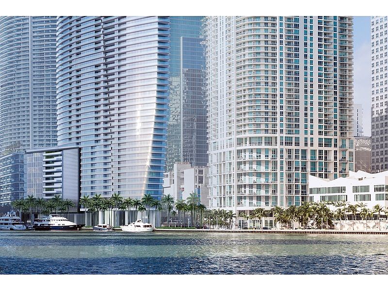 This image showcases a waterfront view of modern high-rise buildings, likely condominiums or apartments, with sleek architectural designs and glass facades. Palm trees line the waterfront, adding a tropical touch, while several boats are docked along the shore. The scene conveys a sense of luxury and urban living by the water.