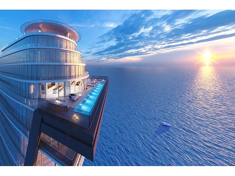 This aerial view showcases a modern, high-rise building with a unique architectural design, featuring curved glass facades and a rooftop infinity pool overlooking the ocean. The building's luxurious amenities and stunning oceanfront location create a sense of exclusivity and high-end living, enhanced by the golden sunset reflecting on the water. A small boat is seen in the distance, emphasizing the vastness of the ocean.