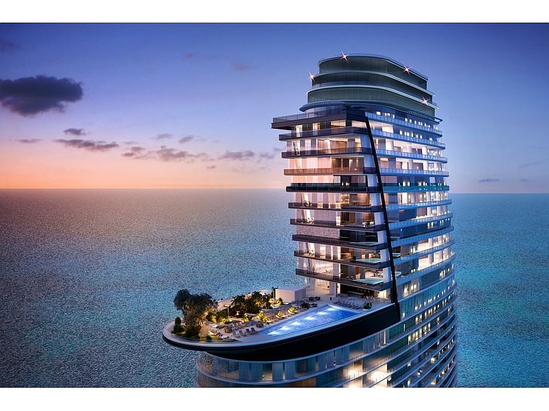 This aerial view showcases a modern, high-rise condominium building situated by the ocean. The building features a unique cantilevered pool deck with lush landscaping and lounge areas. The sleek architectural design and oceanfront location create a luxurious and desirable living environment.