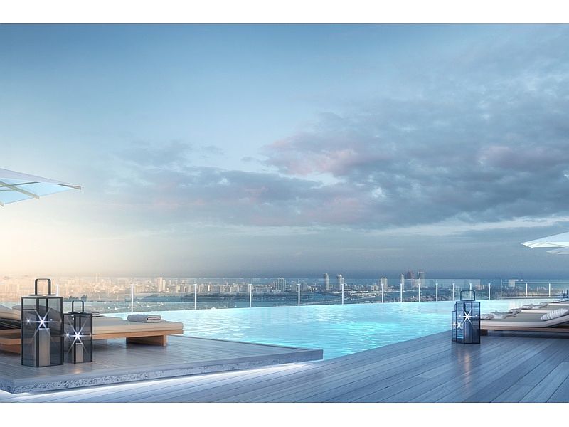 This image showcases a luxurious rooftop infinity pool with stunning city views. The pool is surrounded by a wooden deck with lounge chairs and decorative lanterns, creating a relaxing and upscale atmosphere. The clear glass barrier enhances the sense of openness and provides unobstructed views of the cityscape and sky.