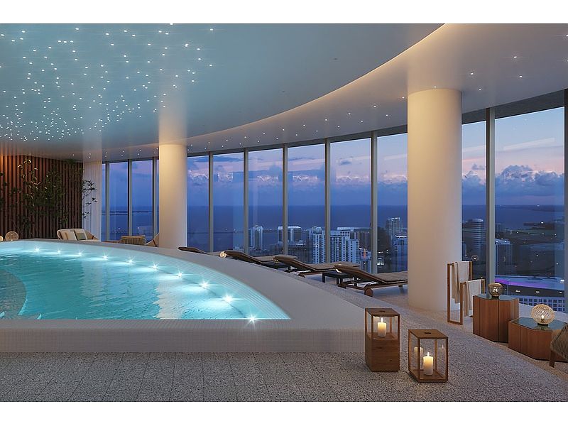 This image showcases a luxurious indoor pool area with floor-to-ceiling windows offering panoramic city and ocean views. The pool features integrated lighting, and the ceiling is adorned with star-like lights, creating a serene ambiance. Lounge chairs and elegant decor enhance the spa-like atmosphere, suggesting a high-end residential amenity.