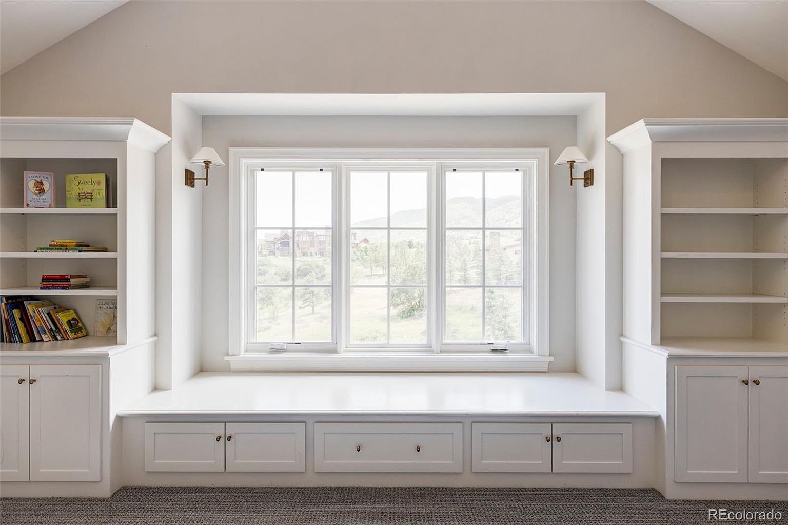This interior shot showcases a charming window seat nestled between built-in bookshelves, creating a cozy and inviting space. The window offers a view of the outdoors, while the surrounding cabinetry provides ample storage and display options. The neutral color palette and natural light enhance the room's serene atmosphere, making it an ideal spot for relaxation or reading.