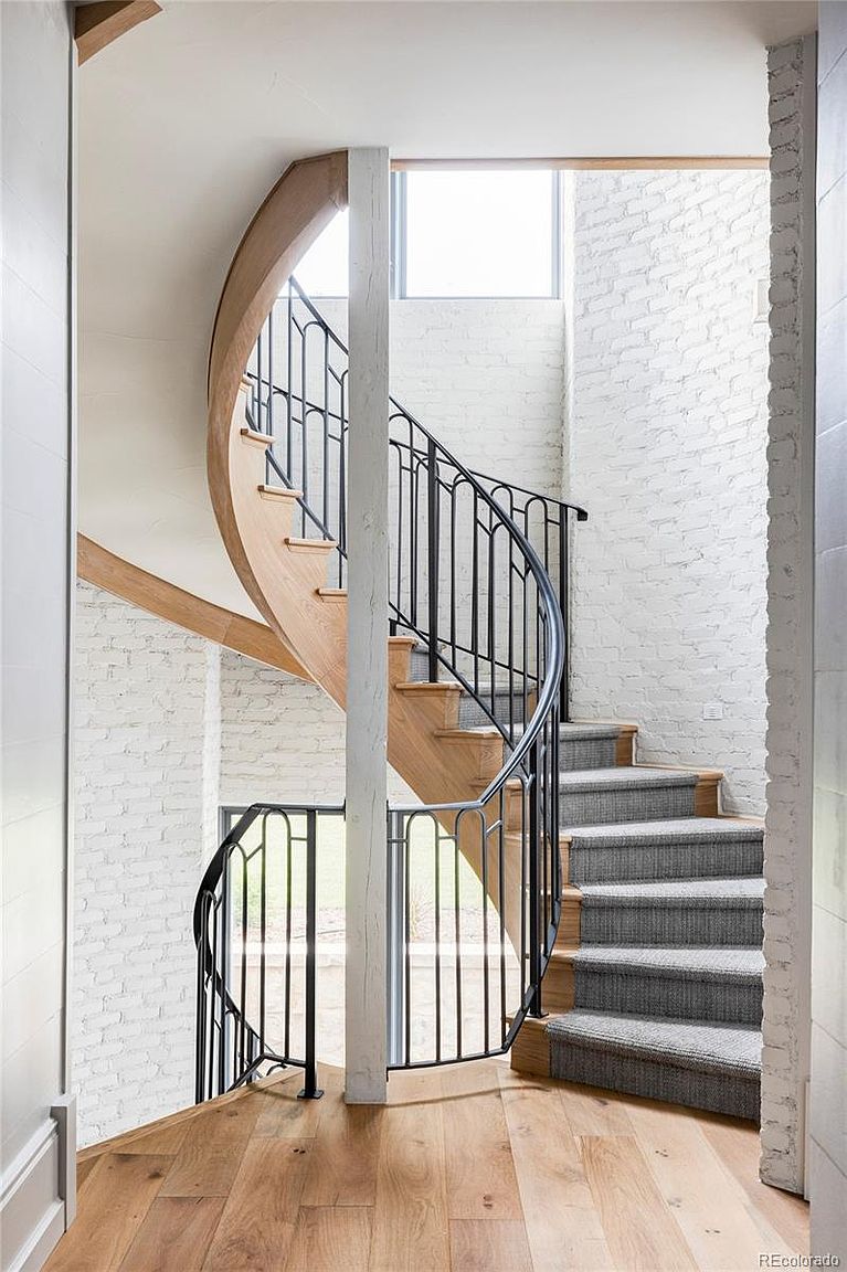 This interior shot showcases a unique staircase design, featuring a combination of carpeted and wooden steps. The staircase is framed by a black metal railing and a white brick wall, creating a modern yet rustic aesthetic. The natural light from the window enhances the architectural details and the overall ambiance of the space.