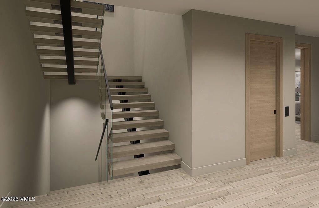 This interior shot showcases a modern staircase with wooden steps and a glass railing, complemented by a black support beam. The hallway features light-colored walls and wooden flooring, leading to a doorway that offers a glimpse into another room. The design is minimalist and contemporary, creating a clean and airy feel.